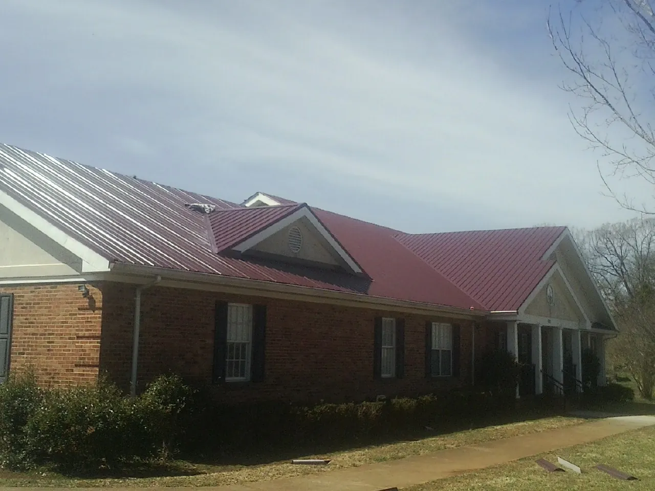 Red metal roof with gabled entries on a long brick building, from a Hail Damage Roof Repair job in Campo