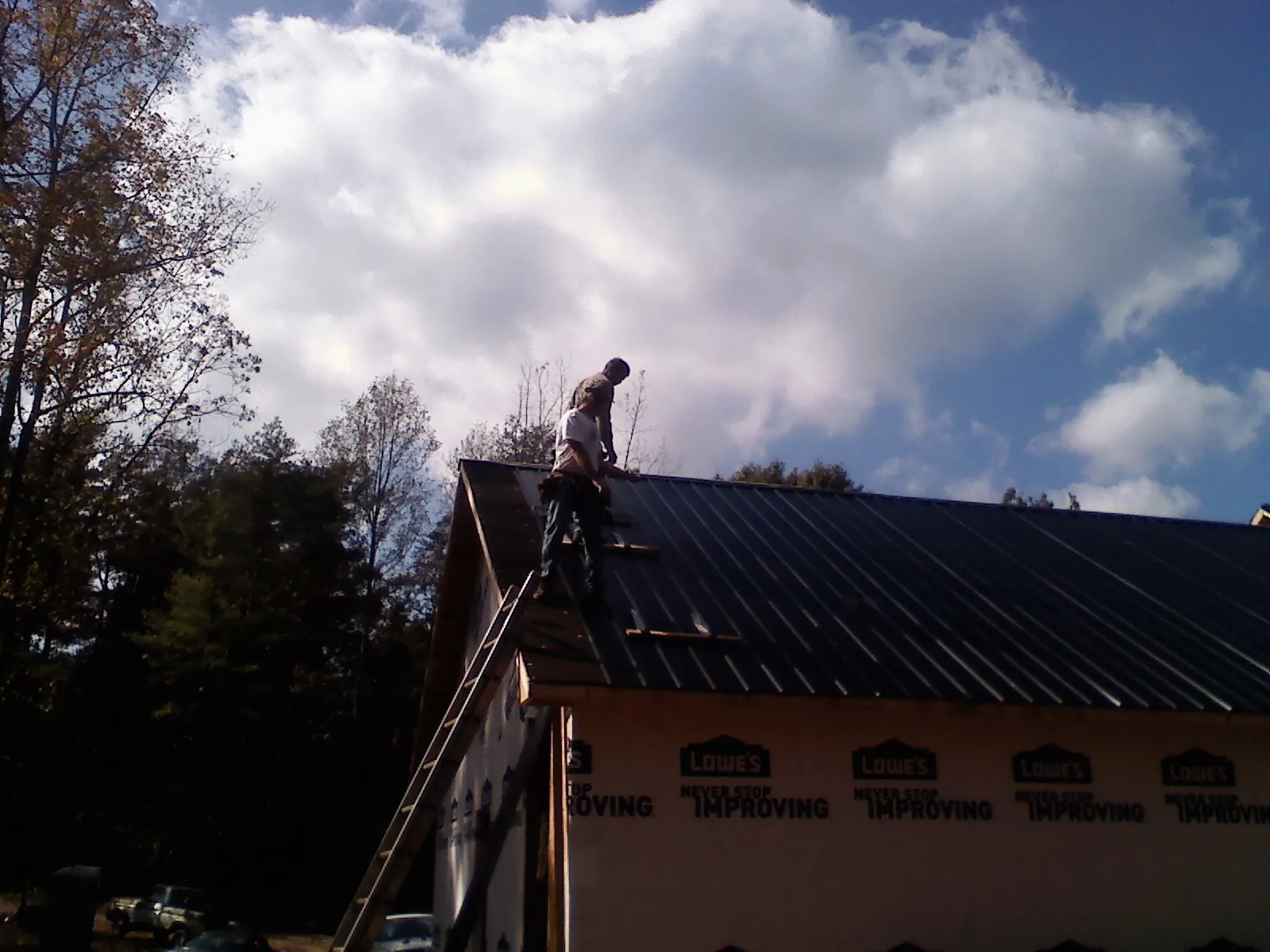 Roofer fastening dark metal panels high against a cloudy sky, from a Roof Inspection job in Campo
