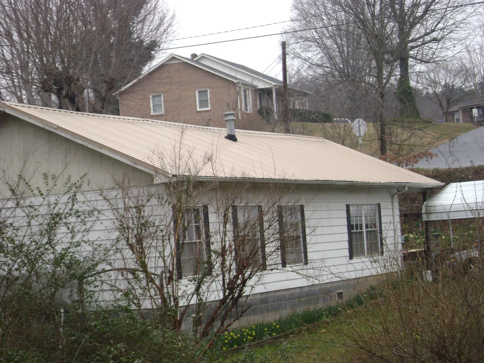 Tan metal roof on a white sided house set into a hillside — Commercial Roofing by Roofing Brothers in Campo